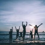 Silhouetted group of friends jumping joyfully on the beach at sunset, symbolizing freedom and happiness.